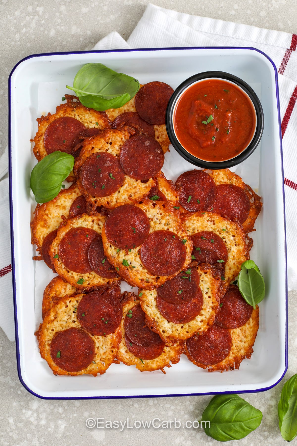 Pizza chips are an easy low carb appetizer made from mozzarella, pepperoni, and simple seasonings. The trick is spacing the cheese mounds so they do not merge, and baking until the edges are browned and golden. Let the chips cool before moving them so they crisp properly. Serve with low carb marinara sauce for dipping, and you have a snack that tastes like pepperoni pizza with a crunchy finish. #easylowcarb plated Pizza Chips with marinara