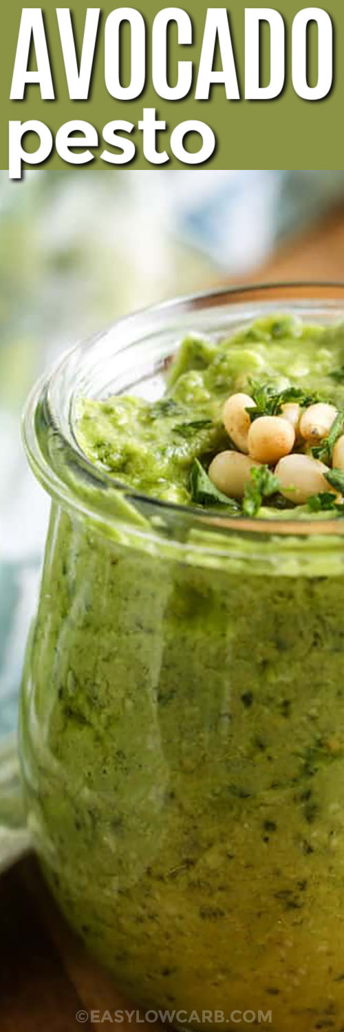 This low carb avocado pesto sauce is rich, herby, and easy to make with fresh basil and ripe avocado. Lemon juice helps brighten the flavor, parmesan adds savory depth, and pine nuts give it a classic pesto taste. Spoon it over zoodles, spaghetti squash, grilled shrimp, chicken, or roasted cauliflower for a fresh sauce that makes simple ingredients taste special. #easylowcarb jar of Avocado Pesto with pine nuts and a title