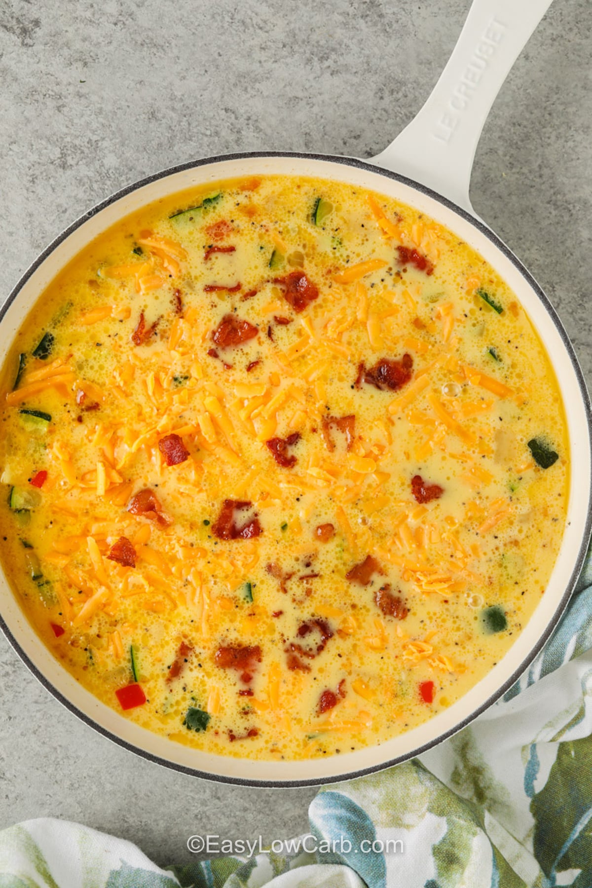 Try zucchini frittata for a satisfying low carb breakfast packed with bacon, cheddar, and colorful vegetables. The eggs bake up light and tender while the zucchini adds fresh flavor to every bite. This zucchini breakfast recipe is perfect for feeding family or enjoying leftovers later in the week. Put this recipe on your table today. #easylowcarb Zucchini Frittata in the pan before cooking