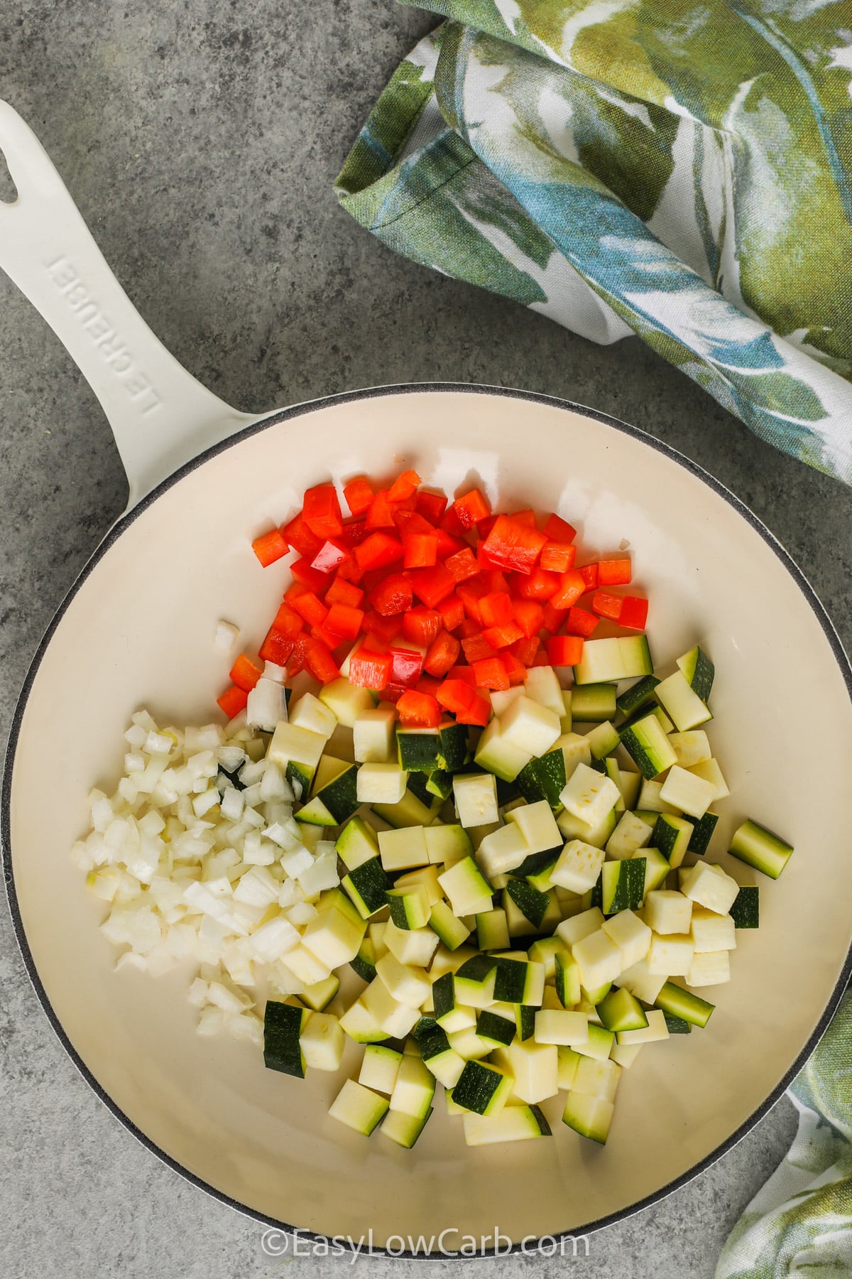 This zucchini frittata is filled with smoky bacon, fresh zucchini, and melty cheddar for a breakfast everyone will love. Every slice is packed with vegetables and rich egg flavor, making it a delicious low carb breakfast recipe. It is a great way to use fresh zucchini while keeping meals satisfying and simple. Save this zucchini frittata recipe and make it soon. #easylowcarb adding veggies together in pan to make Zucchini Frittata