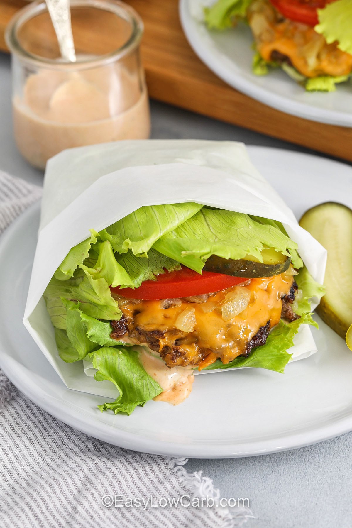 This lettuce wrap burger has a juicy skillet-seared beef patty, melted cheese, crisp pickles, tomato, creamy low-carb sauce, and optional caramelized onions. Several overlapping iceberg or butter lettuce leaves create a fresh, crunchy wrap that holds the classic burger toppings without a bun. It is a simple low carb dinner for busy weeknights, summer cookouts, or casual family meals. Save this easy burger recipe for your next burger night. #easylowcarb plated Lettuce Wrap Burger