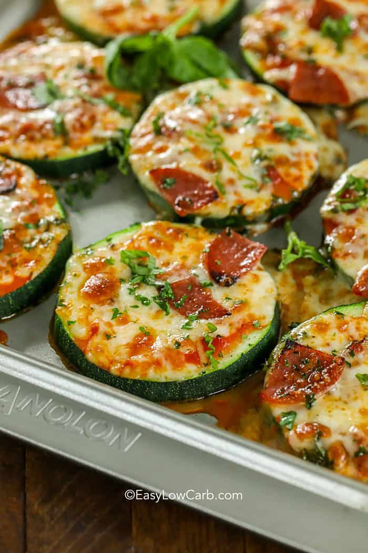 Keto zucchini pizza bites make fresh zucchini taste so delicious with tomato sauce, oregano, mozzarella, and parmesan. Add mini pepperoni, cooked sausage, olives, jalapeños, or finely diced peppers to create different flavors on one baking sheet. The rounds bake until tender before a quick broil melts and browns the cheese. Save this flexible low carb snack recipe for easy entertaining or busy afternoons. #easylowcarb Zucchini Pizza Bites on a sheet pan