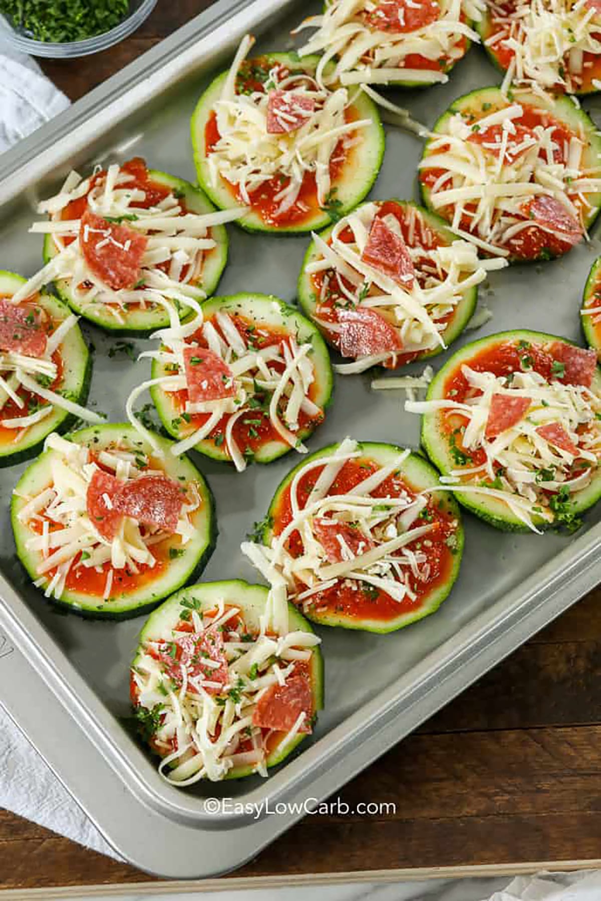 Easy zucchini pizza rounds have all the saucy, cheesy comfort of pizza in a simple low carb, bite-sized form. Wide zucchini slices hold thick pizza sauce, fragrant oregano, shredded mozzarella, parmesan, and favorite toppings without requiring a crust. They cook quickly on a baking sheet and finish under the broiler for golden, bubbling cheese. Pin this low carb pizza appetizer for game day, family movie night, or quick snacks. #easylowcarb Zucchini Pizza Bites on sheet pan before cooking