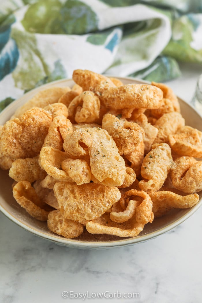 These tasty ranch flavored pork rinds are so simple to make in the air fryer. Three minutes and three ingredients are all you need for this quick and crunchy snack. Just air fry, toss and serve with your favorite dipping sauce for a keto snack that everyone will want to enjoy. Try them for your next games night or keto potluck treat. #easylowcarb ranch seasoned air fried pork rinds in a bowl