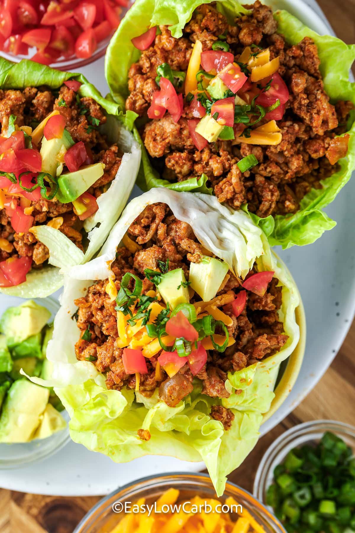 Taco lettuce wraps are packed with seasoned beef, fresh lettuce, and colorful toppings for a meal that is full of flavor. This low carb taco recipe is perfect when you want something satisfying that is also fresh and easy to serve. Everyone can fill their own lettuce cups with favorite toppings for a fun family dinner. Add this recipe to your dinner plans today. #easylowcarb top view of Taco Lettuce Wraps on a plate
