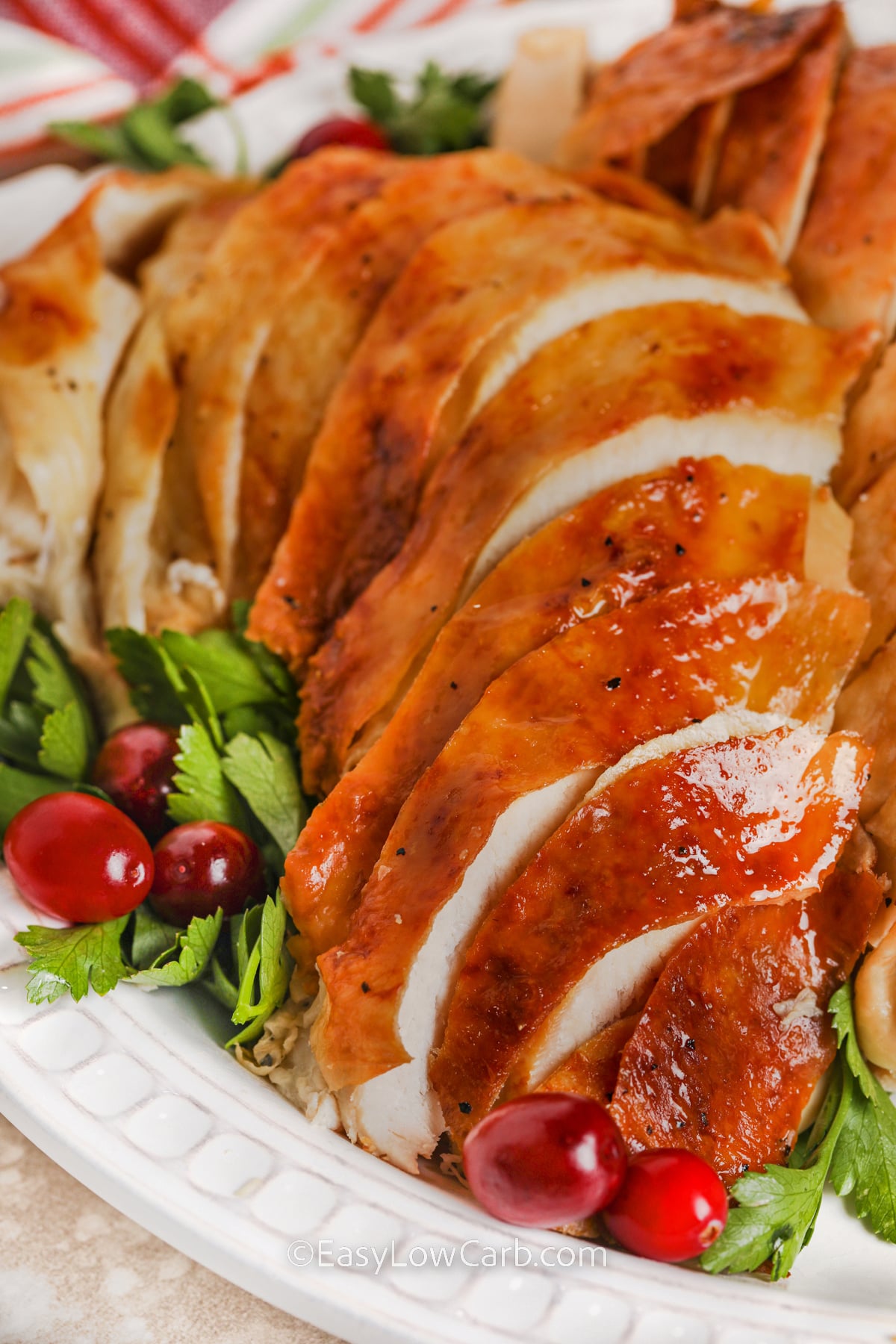 Make an easy oven roasted turkey without complicated marinades or a long ingredient list. This whole bird is coated with butter or oil, seasoned generously, and oven roasted with fresh herbs, garlic, onion, celery, and broth for classic savory flavor. The simple roasting method produces a golden centerpiece that pairs perfectly with low carb vegetables and holiday sides. Pin this easy turkey recipe for Thanksgiving or Christmas. #easylowcarb sliced Oven Roasted Turkey on a plate.