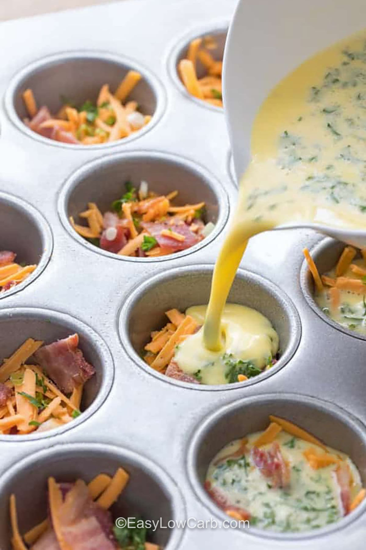 Bacon and egg muffins are a great choice when you want an easy low carb breakfast ready to go. Each muffin is filled with fluffy eggs, savory bacon, cheddar cheese, and green onions for plenty of flavor. Make a batch ahead and store them in the fridge for busy mornings, or freeze extras for later. They are also handy for a quick protein-rich snack. Add these cheesy egg muffins to your meal prep this week. #easylowcarb pouring egg into muffin tin with filling to make Bacon and Egg Muffins