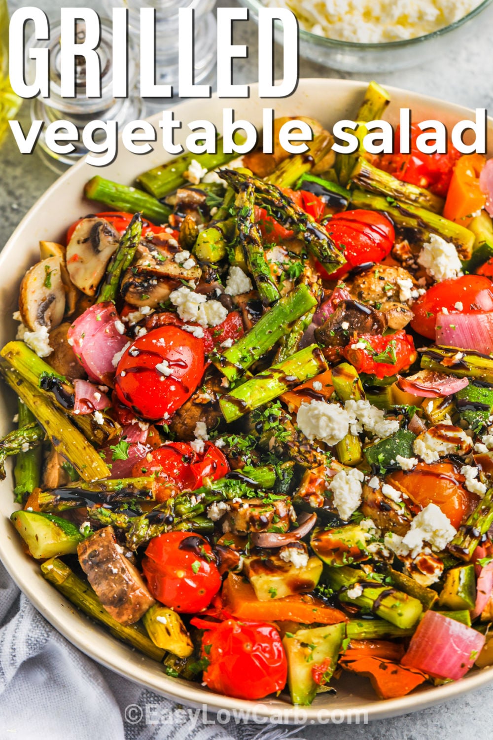 Make an easy grilled vegetable salad with tender-crisp zucchini, asparagus, bell pepper, tomatoes, and red onion. Medium-high heat gives the vegetables lightly charred edges while a lemon and Italian seasoning mixture keeps the flavor bright. Balsamic dressing, feta cheese, and toasted nuts add tang, creaminess, and crunch without making the salad heavy. Add this quick low carb side to your summer meal plan and save the recipe today. #easylowcarb bowl of Grilled Vegetable Salad with a title
