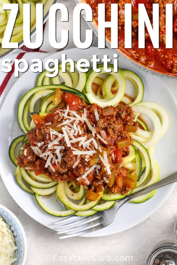 Zucchini spaghetti is a delicious low-carb dinner that brings classic pasta flavor to the table. Tender zucchini noodles are topped with hearty ground beef, tomato sauce, onions, garlic, and green pepper for a satisfying meal. A sprinkle of Parmesan adds the perfect finishing touch. Make this easy zucchini noodle recipe for a family-friendly dinner everyone will enjoy. #easylowcarb top view of Zucchini Spaghetti on a plate with a title.