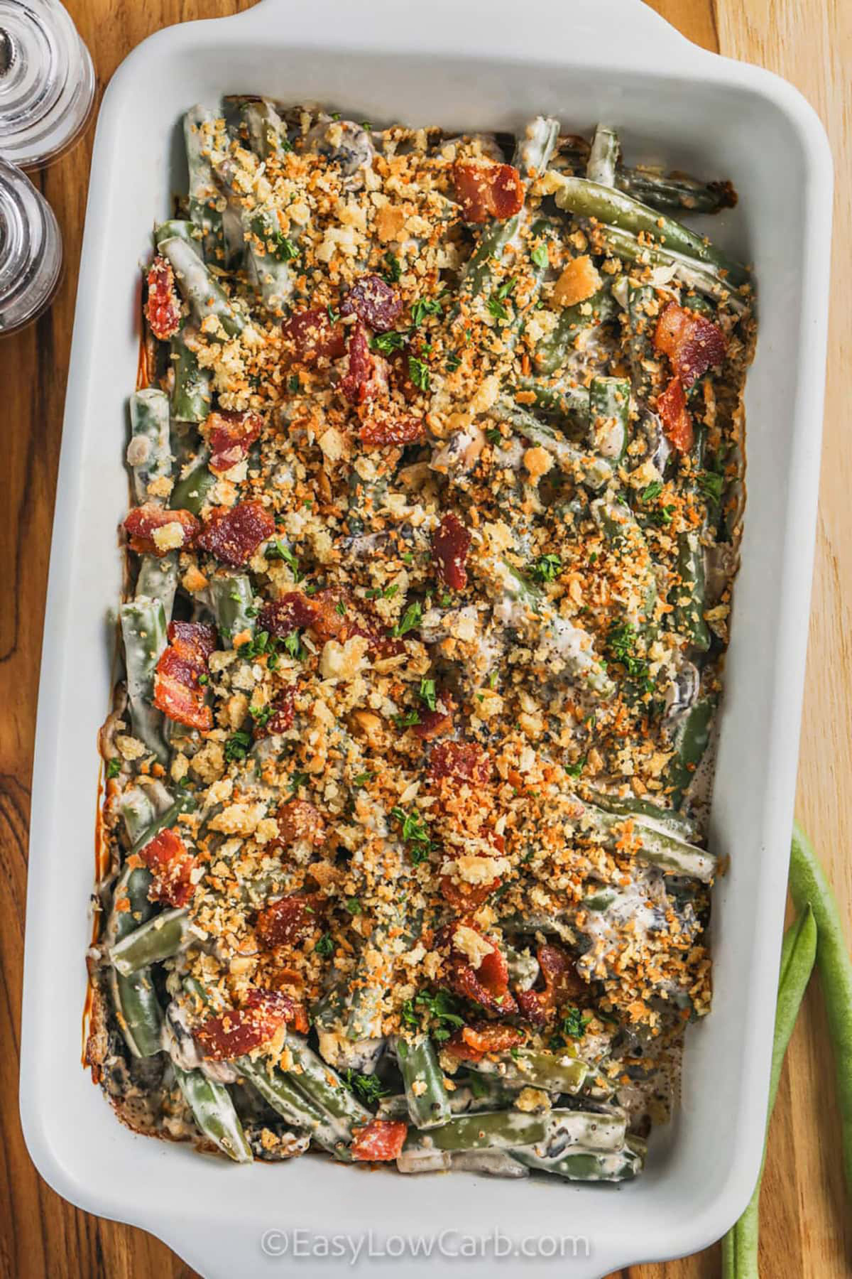 Keto green bean casserole makes a delicious low carb addition to any holiday spread. Green beans are paired with tender mushrooms, crispy bacon, garlic, and a creamy Parmesan cheese sauce for a comforting side dish. The optional keto bread crumb topping adds a tasty finishing touch without taking away from the creamy casserole. It is a simple way to serve a classic favorite with fewer carbs. Try this recipe for your next dinner. #easylowcarb creamy Keto Green Beans Casserole in the dish