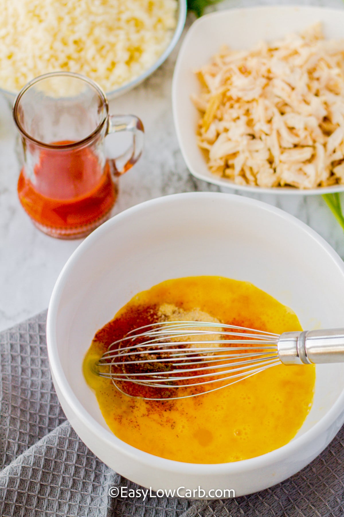 Easy keto buffalo chicken casserole packs all the flavors you love into one satisfying dish. Buffalo sauce adds a spicy kick, while cream cheese, sour cream, and cheddar make the filling rich and savory. Cauliflower rice keeps this casserole low in carbs without leaving it short on flavor. Shredded chicken makes it hearty enough for a family dinner. Try this simple buffalo chicken recipe when you need something delicious. #easylowcarb adding ingredients together to make sauce for Keto Buffalo Chicken Casserole.