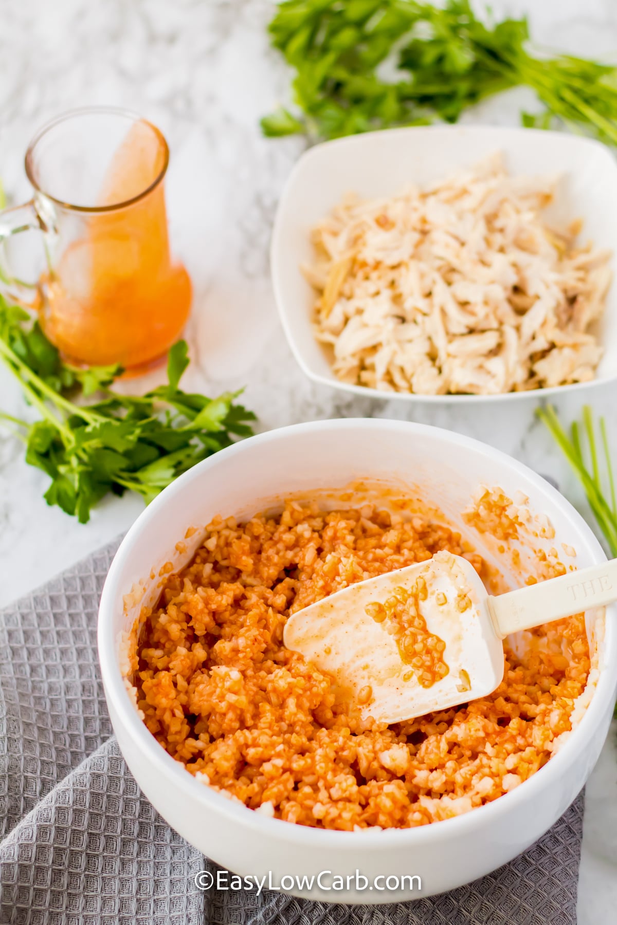 A keto buffalo chicken casserole is just right for anyone craving a spicy, cheesy dinner. It combines cooked chicken with cauliflower rice and a creamy buffalo-seasoned mixture for a filling low-carb meal. Cheddar melts over the top, while optional blue cheese and green onions add extra flavor. It is also a smart way to use leftover rotisserie chicken. Add this easy chicken casserole to your dinner plans. #easylowcarb shredded chicken in a bowl with a bowl of buffalo mixture to make Keto Buffalo Chicken Casserole.