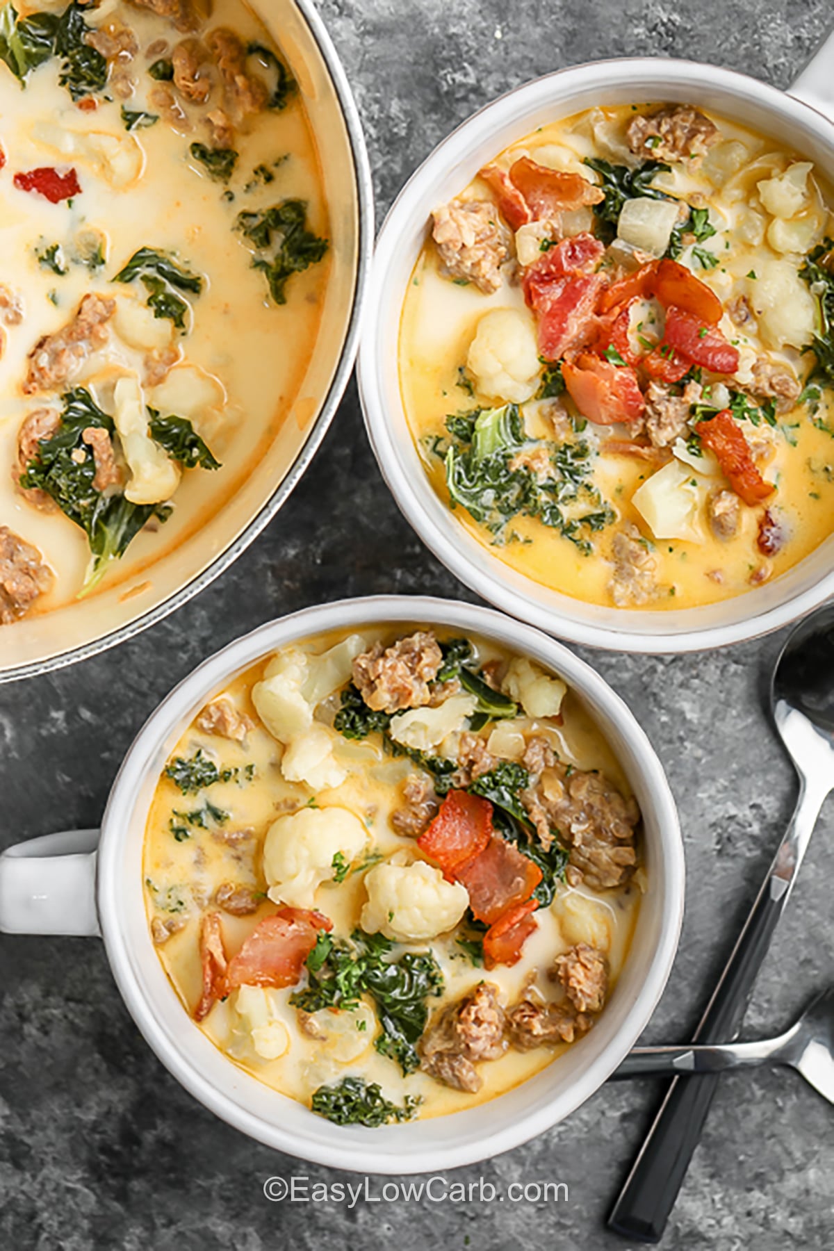 Bring Keto Zuppa Toscana to the table for a cozy meal everyone can enjoy. This hearty soup combines Italian sausage and bacon with cauliflower and kale in a creamy, flavorful broth. It is packed with satisfying ingredients and makes a delicious low carb dinner for cooler evenings. Keep the bacon crispy by adding it just before serving, then finish each bowl with Parmesan if you like. Warm up with this easy keto soup tonight. #easylowcarb savory Keto Zuppa Toscana in bowls.