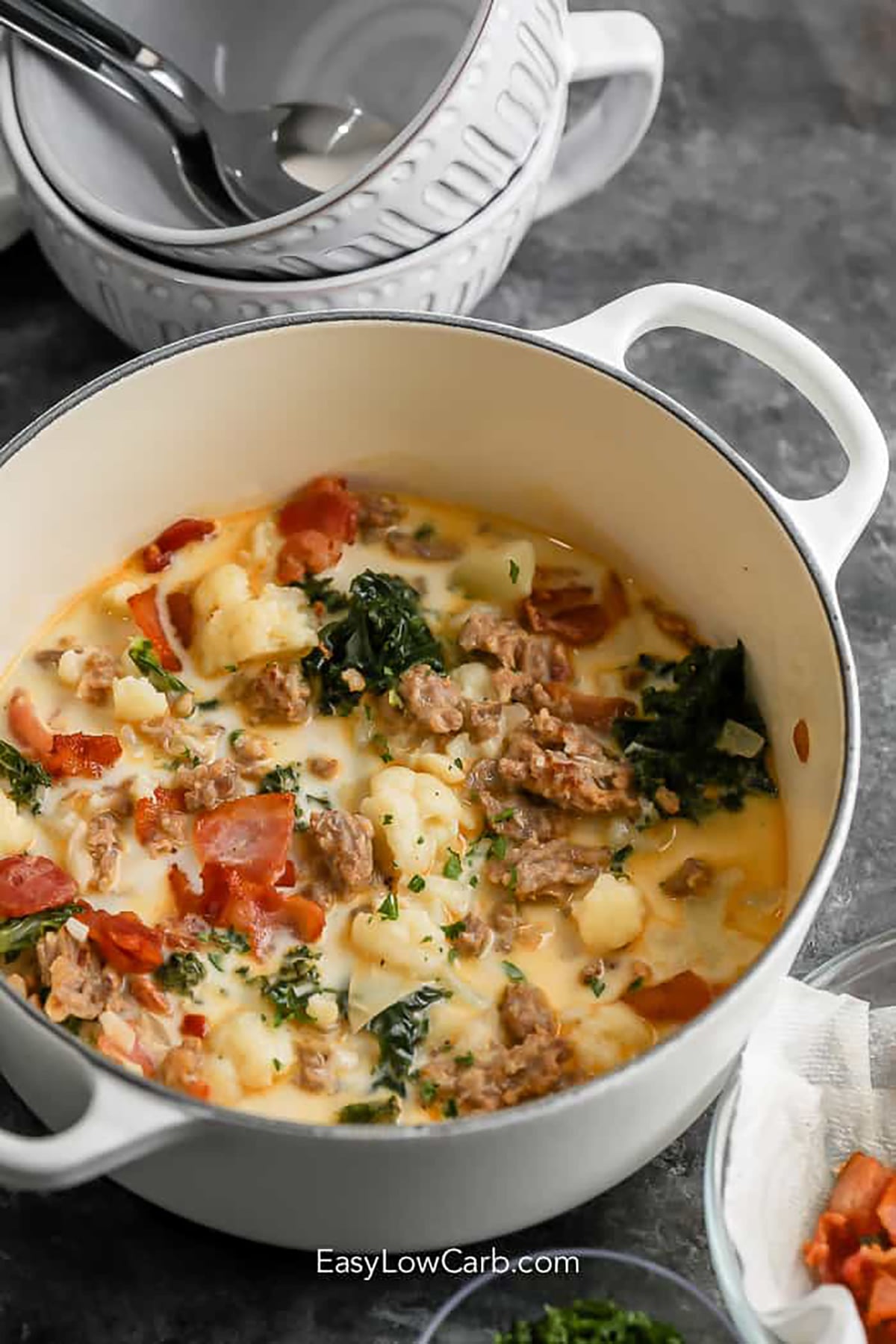Nothing beats Keto Zuppa Toscana when a creamy bowl of soup sounds just right. Savory Italian sausage and bacon pair with tender cauliflower and kale for a hearty combination. The rich broth gets finished with cream for a deliciously satisfying low carb meal. Serve it with Parmesan on top or a simple salad on the side. This easy keto soup is one you will want to keep in your regular dinner rotation. Make it today. #easylowcarb pot of Keto Zuppa Toscana.