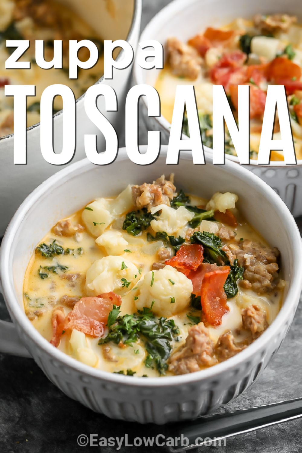 Keto Zuppa Toscana is a creamy, hearty soup filled with Italian sausage, bacon, cauliflower, and kale. The rich chicken broth and cream create a comforting base with plenty of savory flavor in every spoonful. This easy low carb soup makes a satisfying dinner for chilly days and is a delicious way to enjoy Italian-inspired comfort food without the potatoes. Top each bowl with crispy bacon and Parmesan. Try this cozy keto soup tonight. #easylowcarb bowls of Keto Zuppa Toscana with a title.